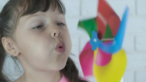 Young Girl Blowing on Colorful Pinwheel Indoors