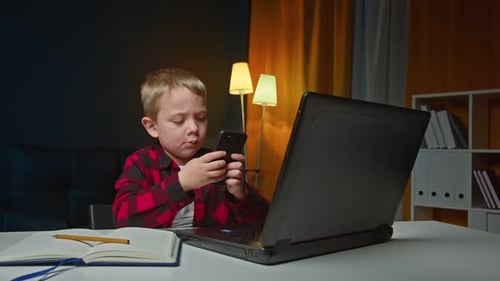 Boy Uses Cell Phone While Sitting At Desk