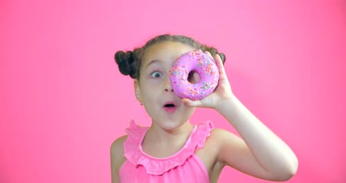 Attractive Cute Little Girl Holding Donuts with Icing To Her Hands Smiling Looks at the Camera and