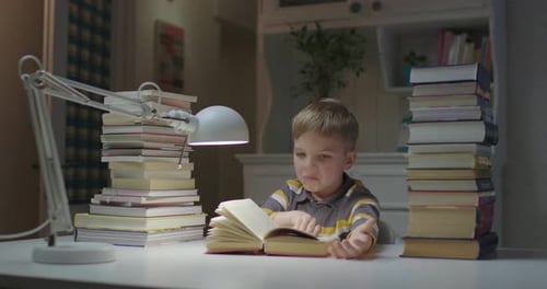 Boy Reading Book at Desk Surrounded by Books