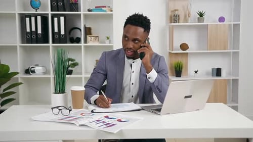 Young Adult Works at Desk Taking Notes on Phone