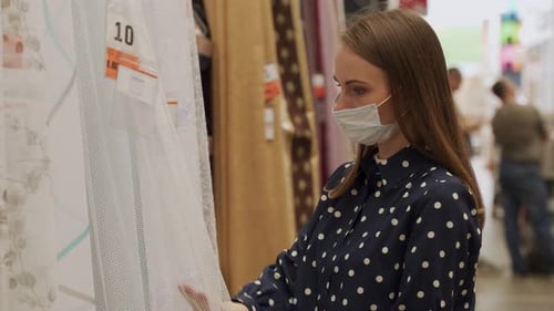 Young Woman in a Protective Mask Chooses New Curtains in a Store