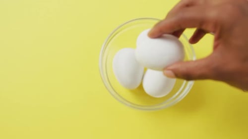 Video of close up of biracial man putting egg into bowl on yellow background