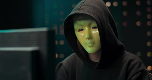 Masked Hacker Typing at Computer in Dark Room