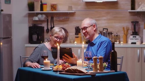 Senior Couple Using Tablet at Candlelit Dinner