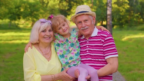 Little Cute Granddaughter Child Embracing with Her Grandmother and Grandfather Family Couple in Park