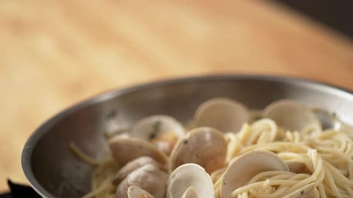La caméra suit la cuisson des pâtes aux palourdes dans une poêle. Ralenti.