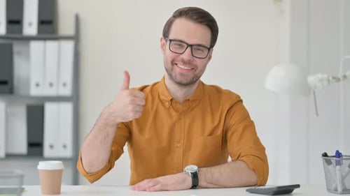 Man Smiling and Giving a Thumbs Up at Desk