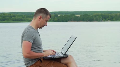 Handsome Man Sitting on a Wooden Pier With Laptop