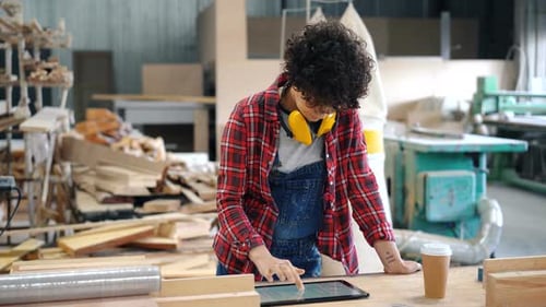 Pretty Girl Using Tablet in Wood Workshop and Looking Around Busy with Device