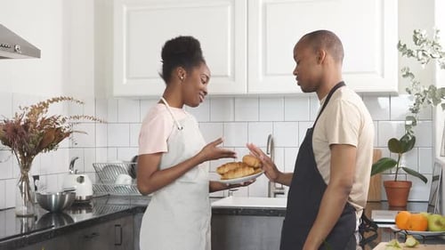 Woman Presents Croissants to Man in Kitchen
