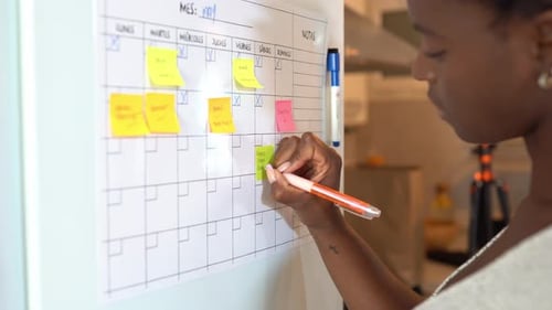 Crop black woman taking notes in planner on fridge