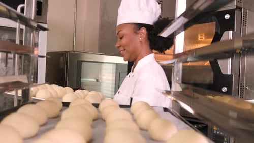 Female Baker Putting Bread into Oven in Bakery