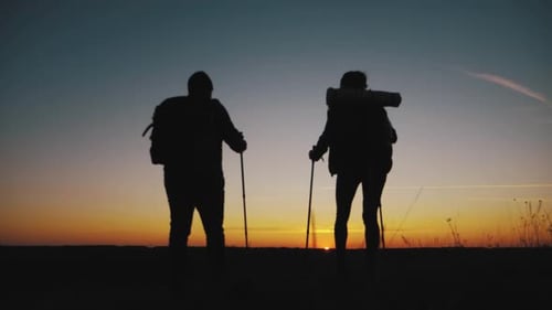 Happy Couple Man and Woman Tourist at Top of Mountain at Sunset Outdoors During a Hike. Silhouettes