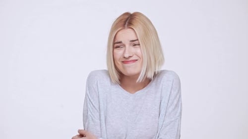 Jeune belle fille blonde timide et embarrassée sur fond blanc, ralenti