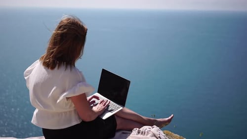 Successful Business Woman in Yellow Hat Working on Laptop By the Sea