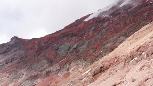 Vue aérienne, survolant une pente avec les pentes rouges et grises d'un volcan en arrière-plan