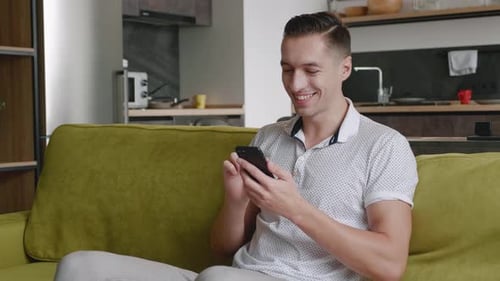 Smiling man on sofa using smartphone at home