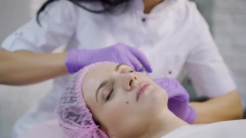 Eine schöne Frau liegt auf einer Couch mit der Kosmetikerin bei einem Mesotherapie-Verfahren