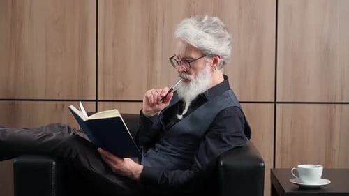 Eleganter grauhaariger Mann arbeitet im Büro, Art Director schreibt Ideen und Konzepte in ein Notizbuch