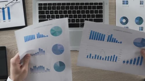 Office Manager Comparing Statistical Reports of Company Typing in Data to Laptop
