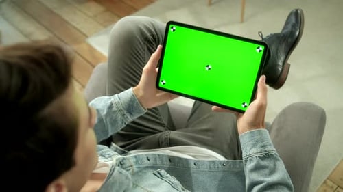 View From the Shoulder of Man Holding and Using Hand Gestures on Green Mock-up Screen Digital Tablet
