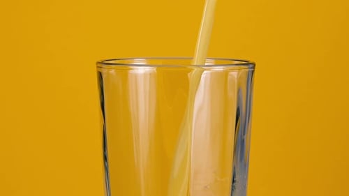 Pouring Orange Juice into Glass on Yellow