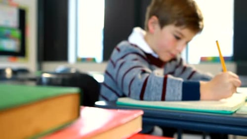 Child Writes with Pencil at School Desk