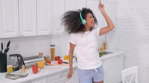 Woman Joyfully Dancing in Bright Kitchen with Headphones
