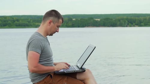 Handsome man sitting on a wooden pier with laptop