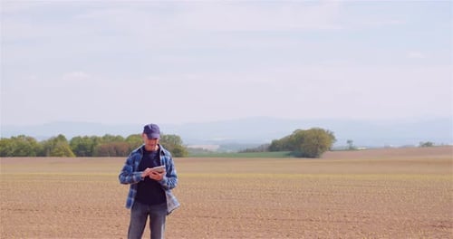 Farmer Examining Agricultural Field While Working on Digital Tablet Computer at Farm.