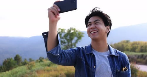 Young Asian traveler taking video with smart phone on top of the mountain.