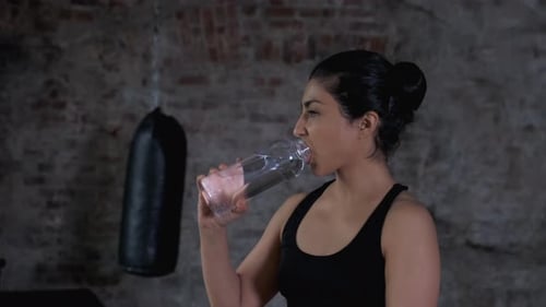Portrait shot of attractive fit woman drinking water after training in the gym.