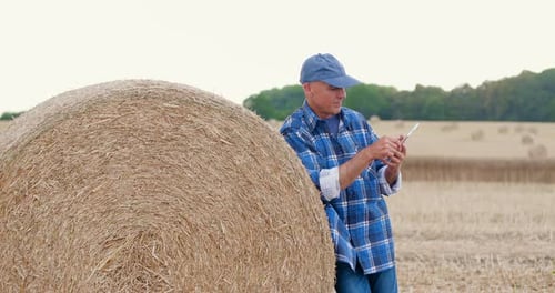 Man Using Tablet in Farm Field by Hay Bale