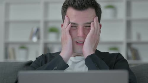 Young Adult Rubbing Face While Using Laptop