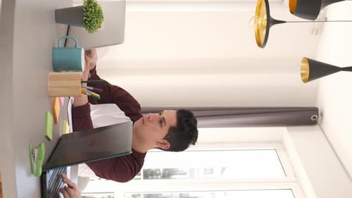 Young Adult Working at Table on Laptop at Home