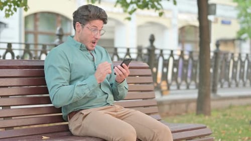 Man Celebrates Using Smartphone on Park Bench