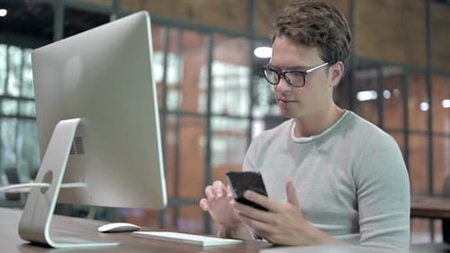 Junger Mann fügt Daten im Computer vom Smartphone hinzu