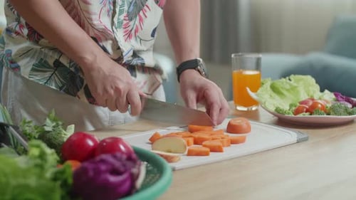 Close Up Of Man's Hands Holding A Knife And Slicing Carrot On The Chopping Board At Home