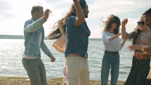 Groupe multifacial d'amis hommes et femmes dansant sur la plage près d'un magnifique lac en été