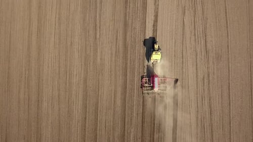 Top down aerial view of green tractor cultivating ground and seeding a dry field. Farmer preparing