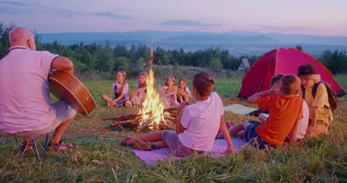 Children Around Campfire with Guitar Player at Twilight