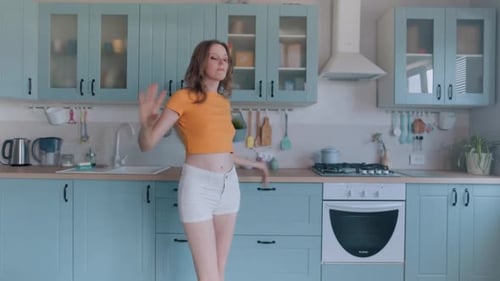 A Beautiful Woman in White Shorts is Relaxing at Home Dancing in the Kitchen