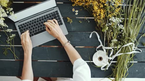 Typing on Laptop Surrounded by Flowers