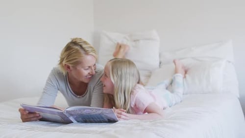 Side view of a Caucasian woman reading a story to her daughter on bed