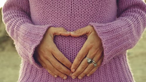 Les mains de la femme font signe de foyer sur le ventre contre un pull violet. Vie romantique et néonatale enceinte