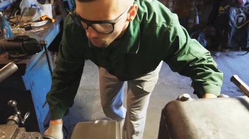 Male Mechanic in Protective Eyewear Uses a Turning Lathe to Processing Metal in Garage