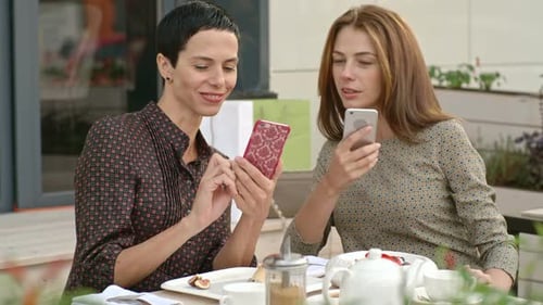 Women Friends Use Phones at Cafe Table