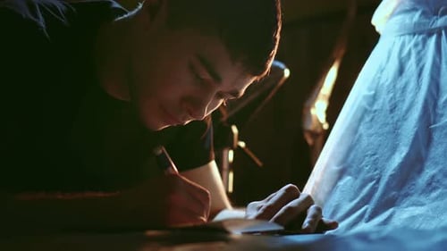 Young Artist Drawing on Paper in Dark Room