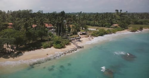 Drone Flying Around Small Idyllic Ocean Resort House with Palm Trees, Waves Washing the Shore with